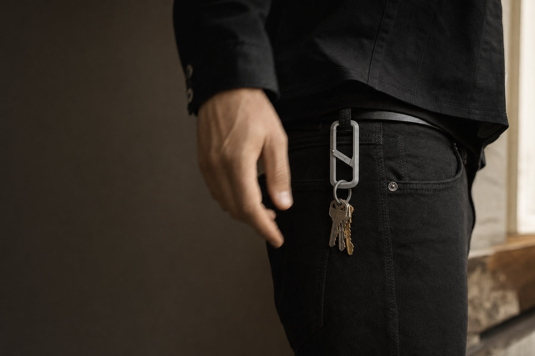 The Madison titanium key carrier clipped to a dark denim belt loop at first light