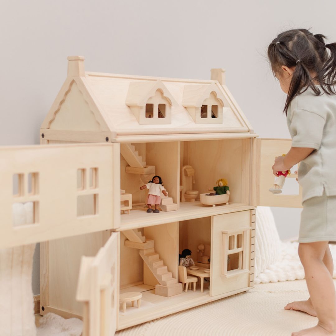 A child bringing the open wooden dollhouse to life with dolls and furniture