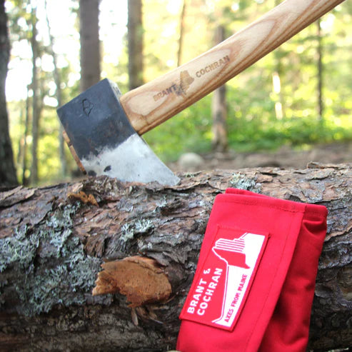 Brant and Cochran axe and red Axe Care Kit roll beside a forest log