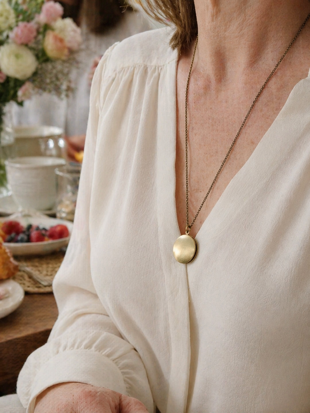Round brushed brass locket necklace worn over an ivory blouse