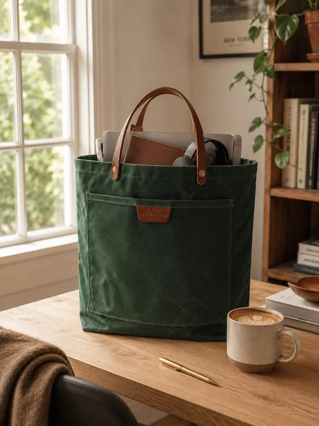 Coal Tote on a sunny desk holding a laptop, leather notebook and headphones beside a latte.