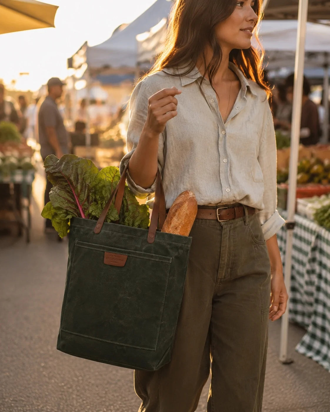A woman carries the Coal Tote, loaded with greens and a baguette, through a sunlit farmers market.
