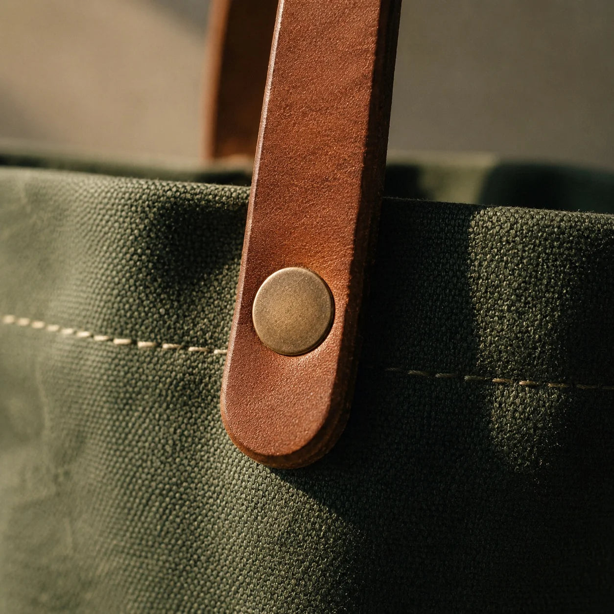 Macro detail of the tan leather handle riveted to the canvas with a solid brass rivet and waxed-thread stitching.