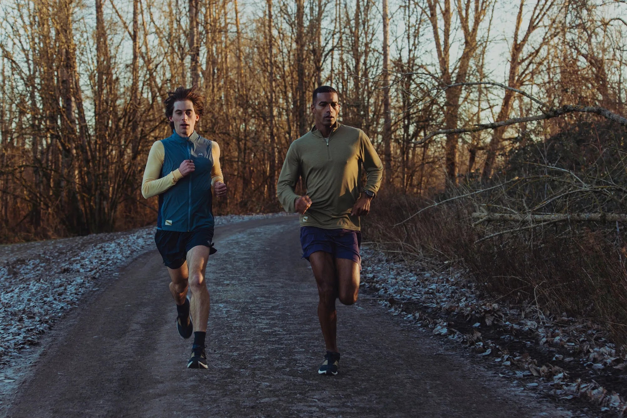 Two runners on a frosted road through bare winter trees at sunrise