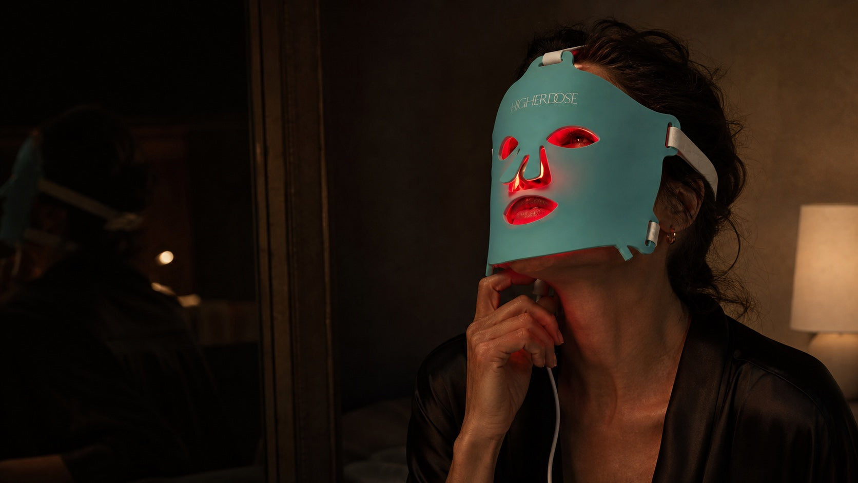 Woman wearing the turquoise HigherDOSE red light mask during a quiet nighttime ritual