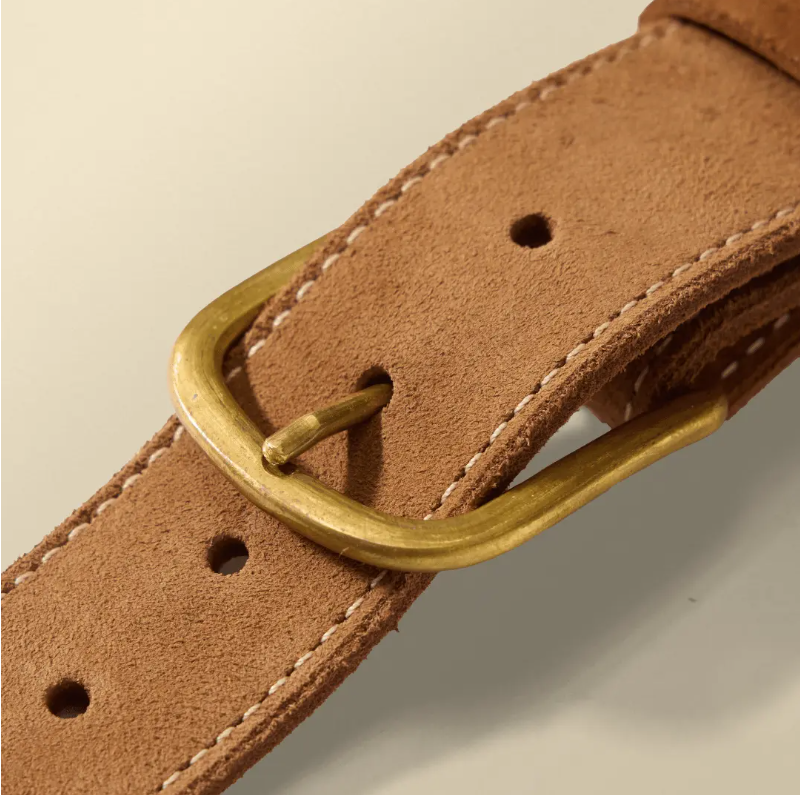 Macro view of the belt's brown roughout texture, contrast stitching, and brass buckle